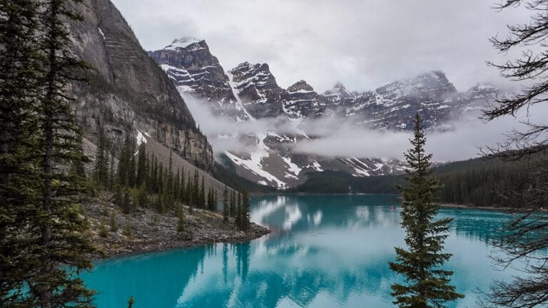 Turquoise lake with reflections, surrounded by snow-capped mountains and evergreen trees, enveloped in mist. A serene, tranquil landscape, one of the major things to do in banff national park in summer.