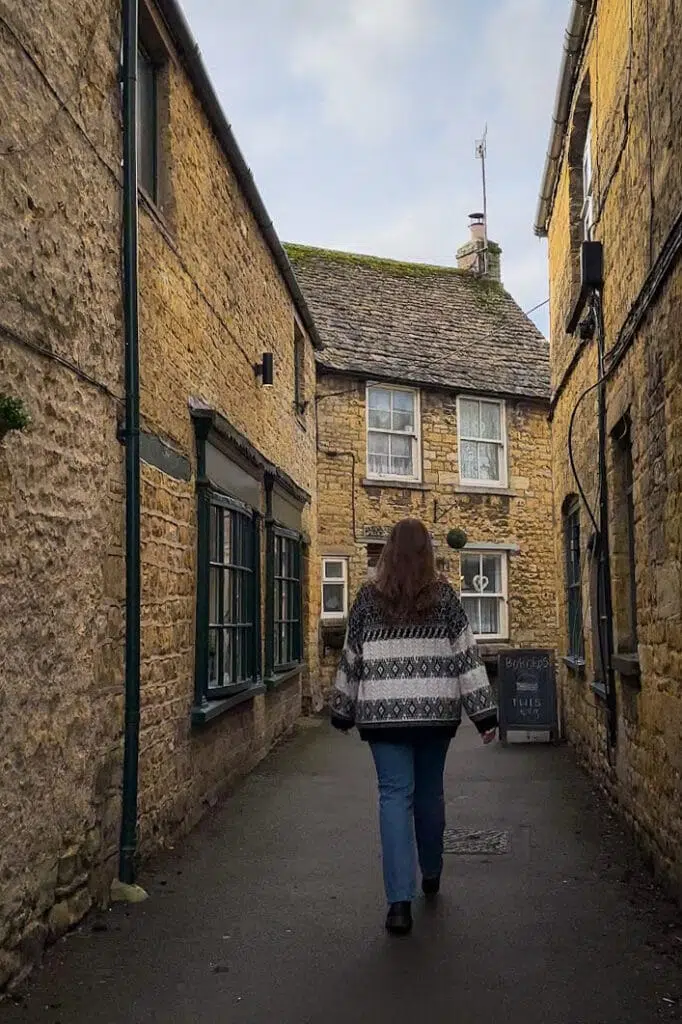 a woman walking down a narrow alley between buildings in Bourton on the Water Cotswolds UK