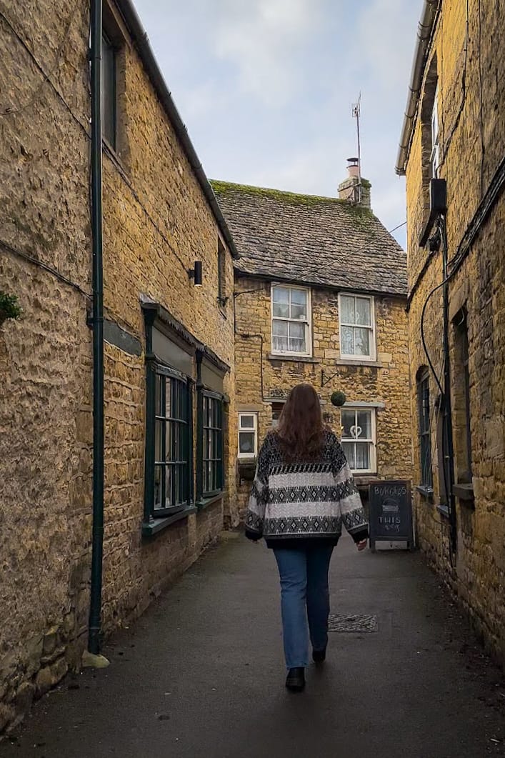 a woman walking down a narrow alley between buildings in Bourton on the Water Cotswolds UK
