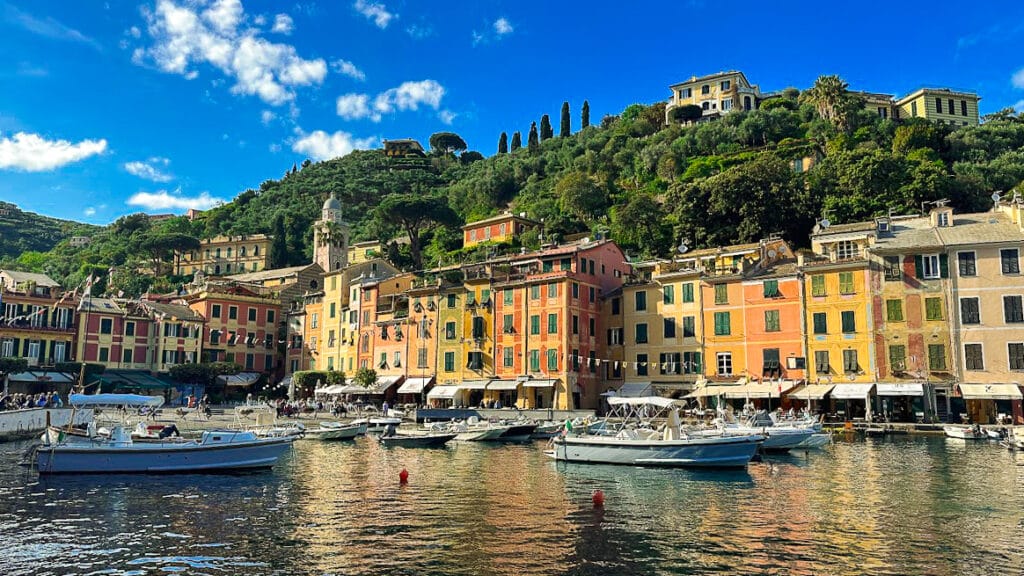Mediterranean village at top destination in italy with colorful buildings by a harbor, surrounded by lush hills. Boats float on calm water under a vibrant blue sky, creating a serene atmosphere.