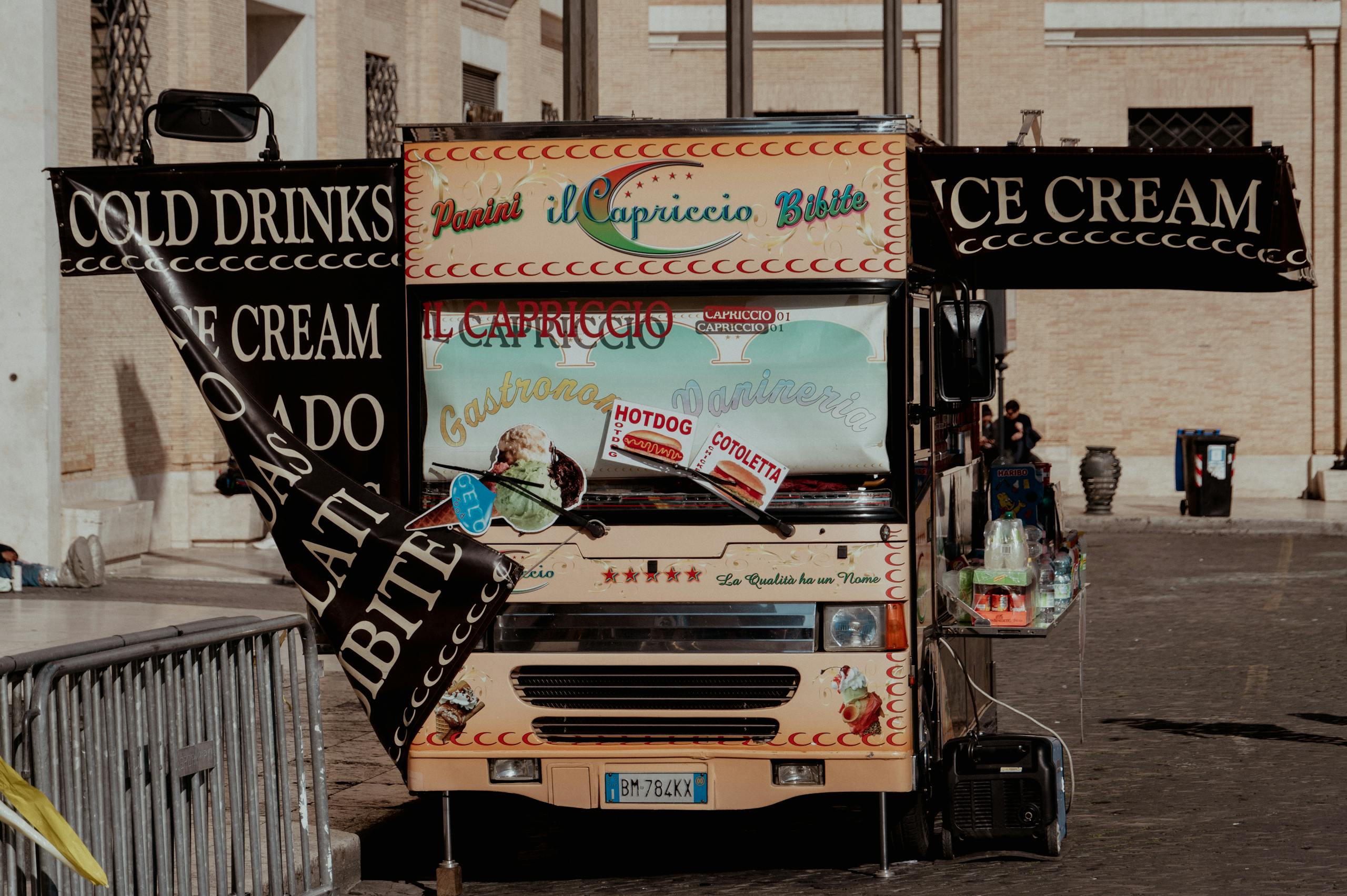 A charming food truck in Rome offering cold drinks and ice cream on a sunny day in an urban setting.