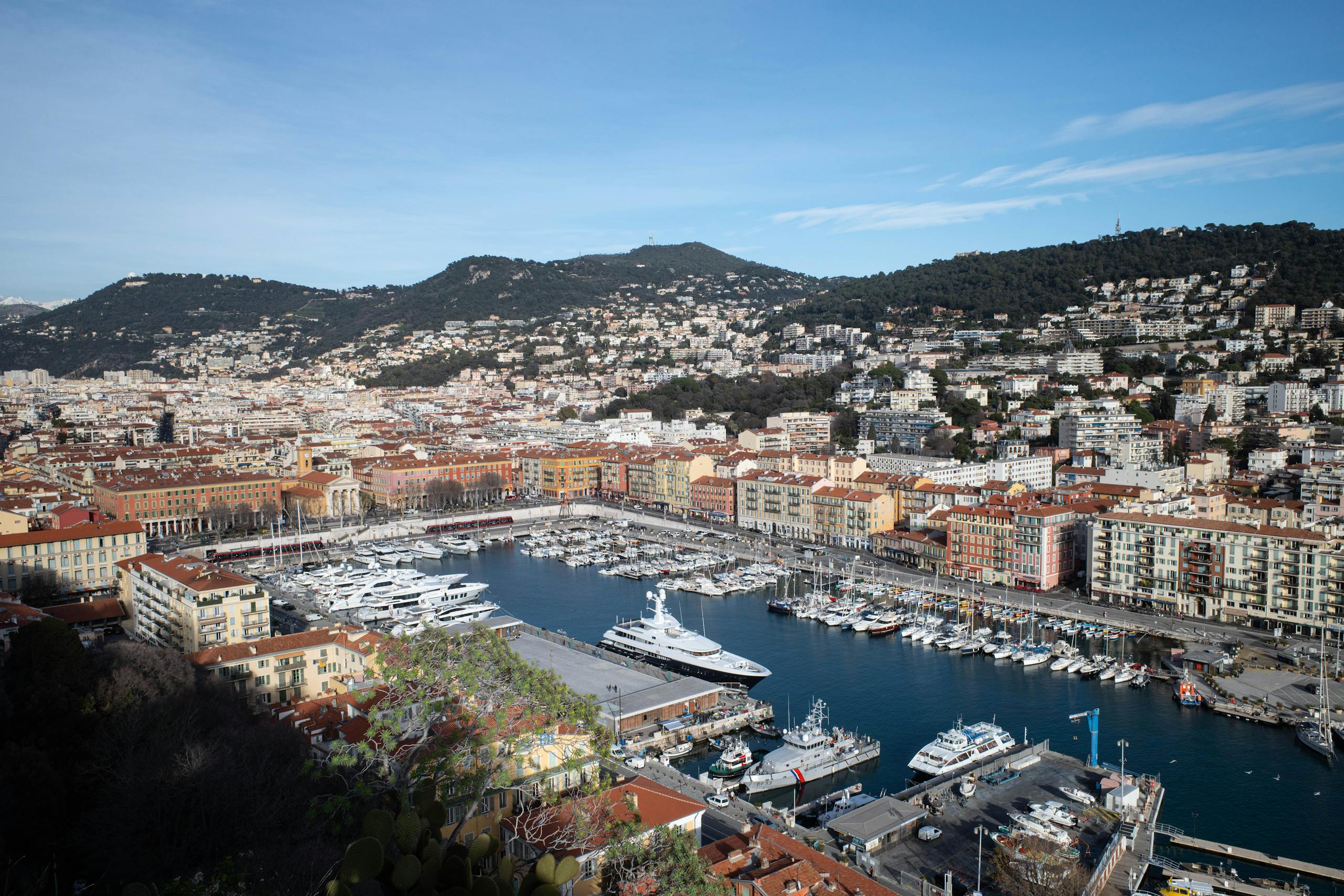A picturesque view of the Nice harbor with yachts and historical buildings under a clear blue sky.