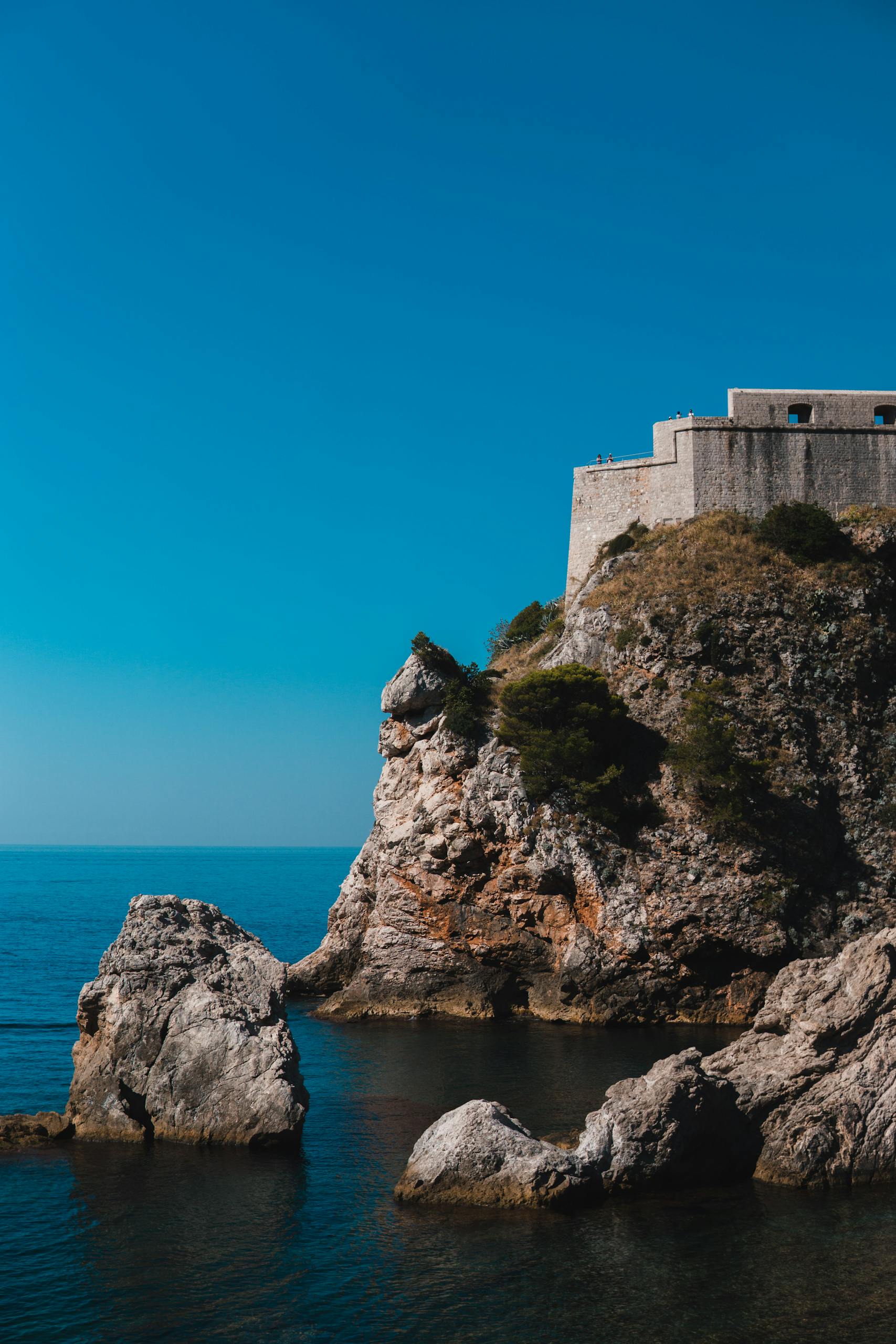 A scenic view of the rocky cliffside and historic fort in Dubrovnik, Croatia, overlooking the sea.