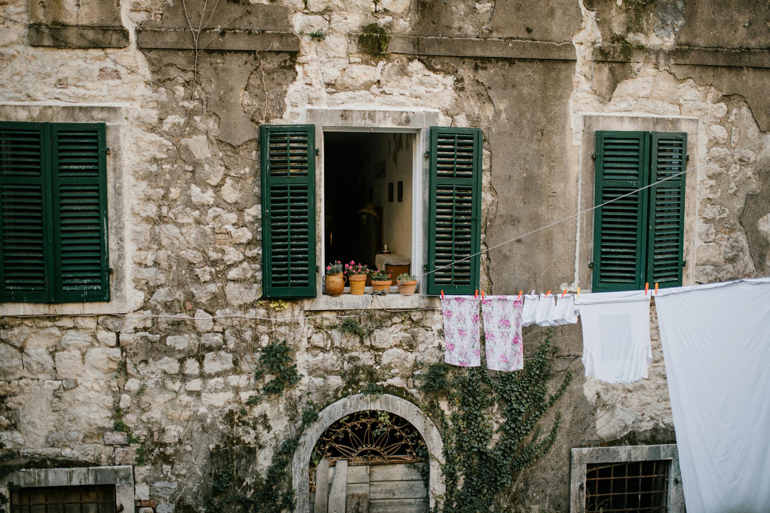Charming stone house facade in Montenegro with plants and clothes drying outside.