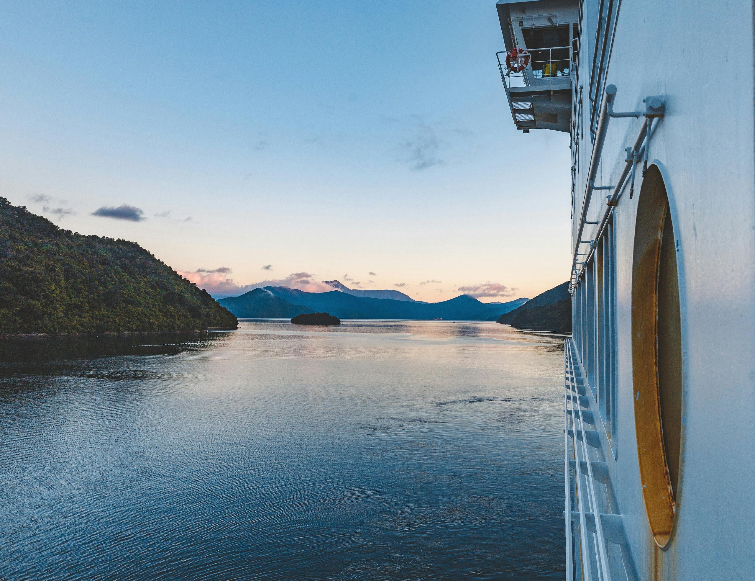 Experience serene sailing in New Zealand's stunning waters with lush landscapes and a tranquil sunrise.