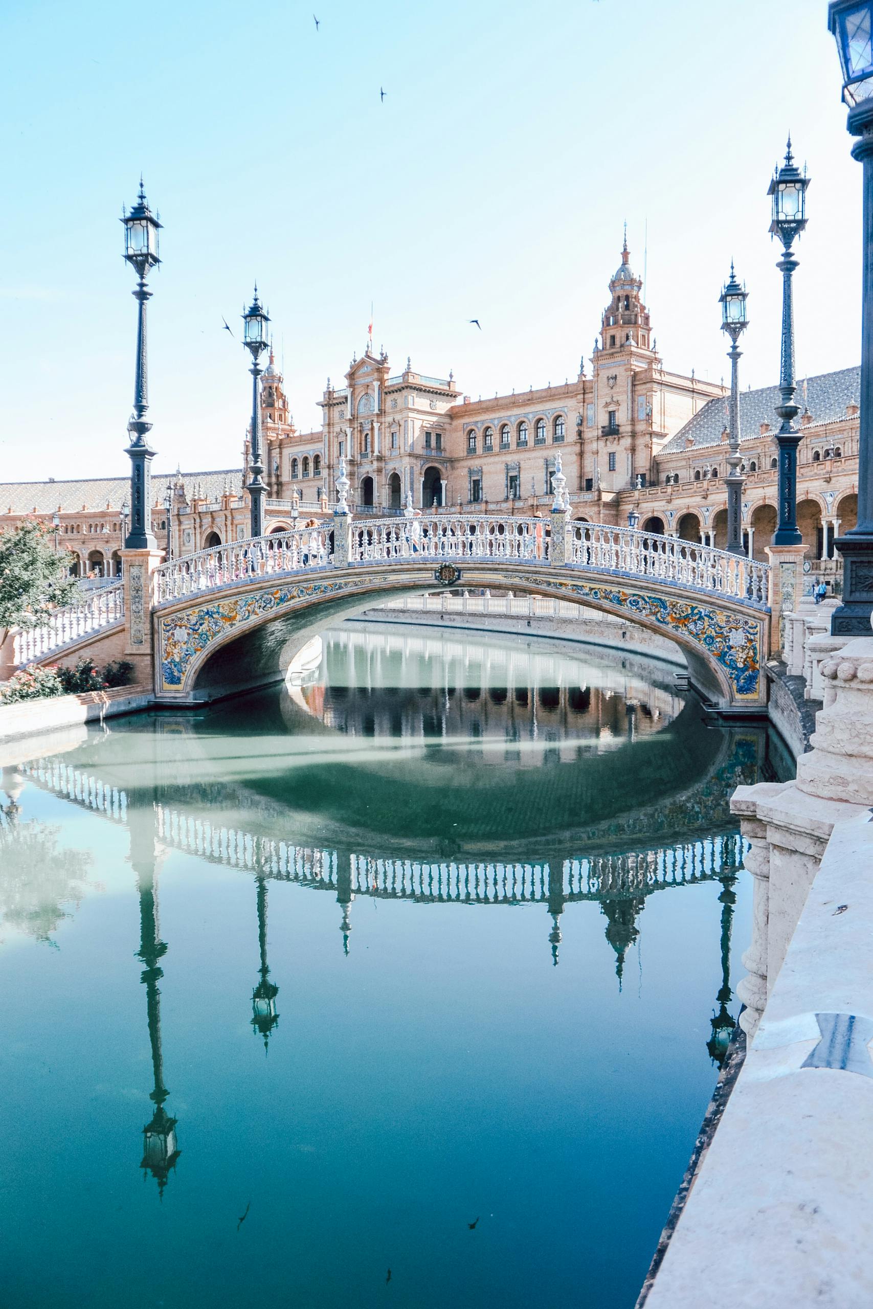 Explore the stunning architecture of Plaza de España in Seville, featuring a beautiful bridge and canal reflection.