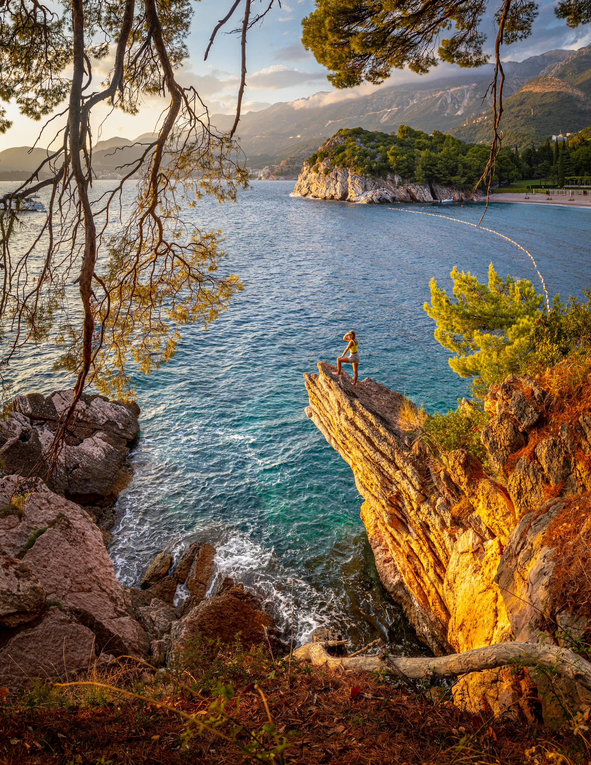 Woman standing on a cliff with a stunning coastal view in Budva, Montenegro during sunset.
