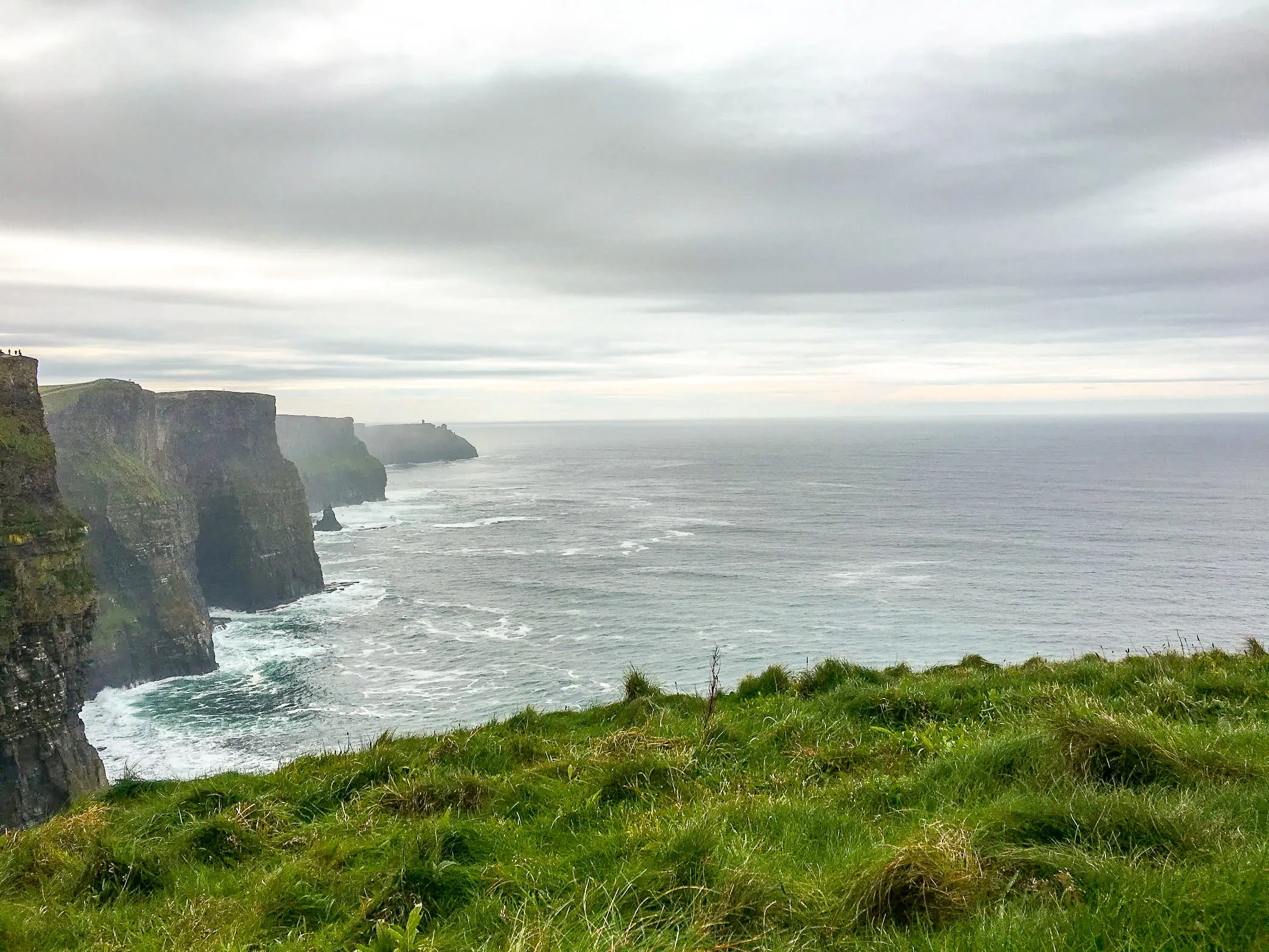 Grass-covered cliffs overlooking a vast ocean under a cloudy sky, as highlighted in the best Ireland travel guide.