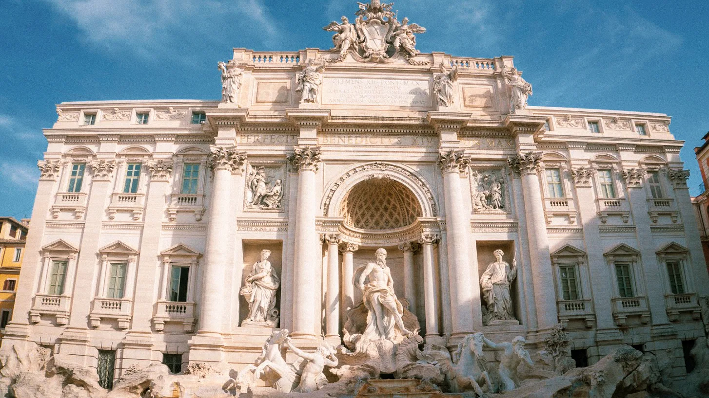 Majestic stone Trevi fountain with intricate carvings, statues of figures and horses, set against an ornate, historic building under a clear blue sky. A stop during the 1 day rome itinerary.
