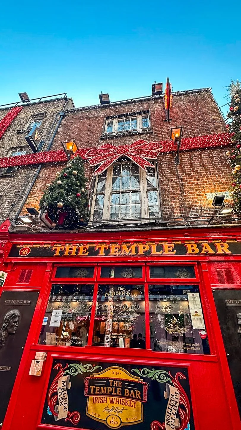 Red facade of The Temple Bar with festive decorations. A brick building with a large bow, greenery, and lights, creating a cheerful holiday atmosphere.