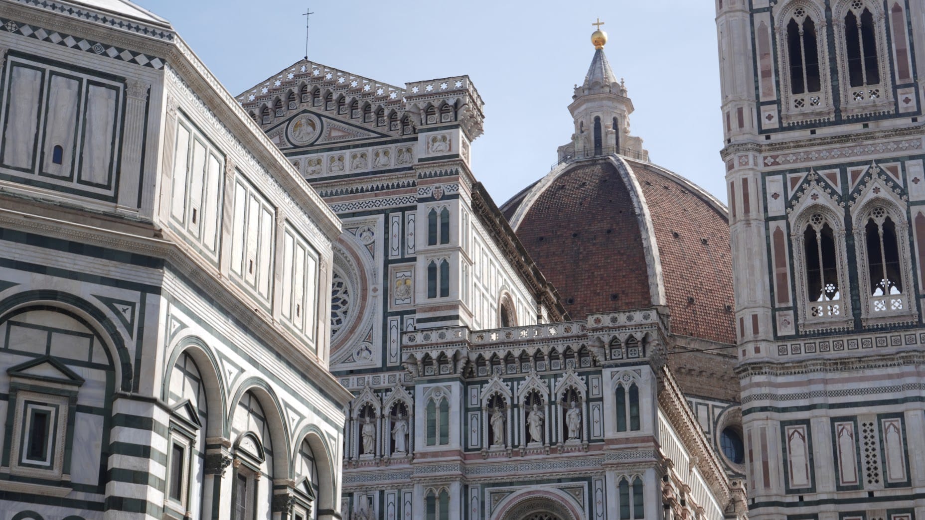 Florence Cathedral's intricate facade with geometric patterns of white, green, and pink marble, crowned by a massive red-tiled dome under clear blue sky in where to stay in florence italy.