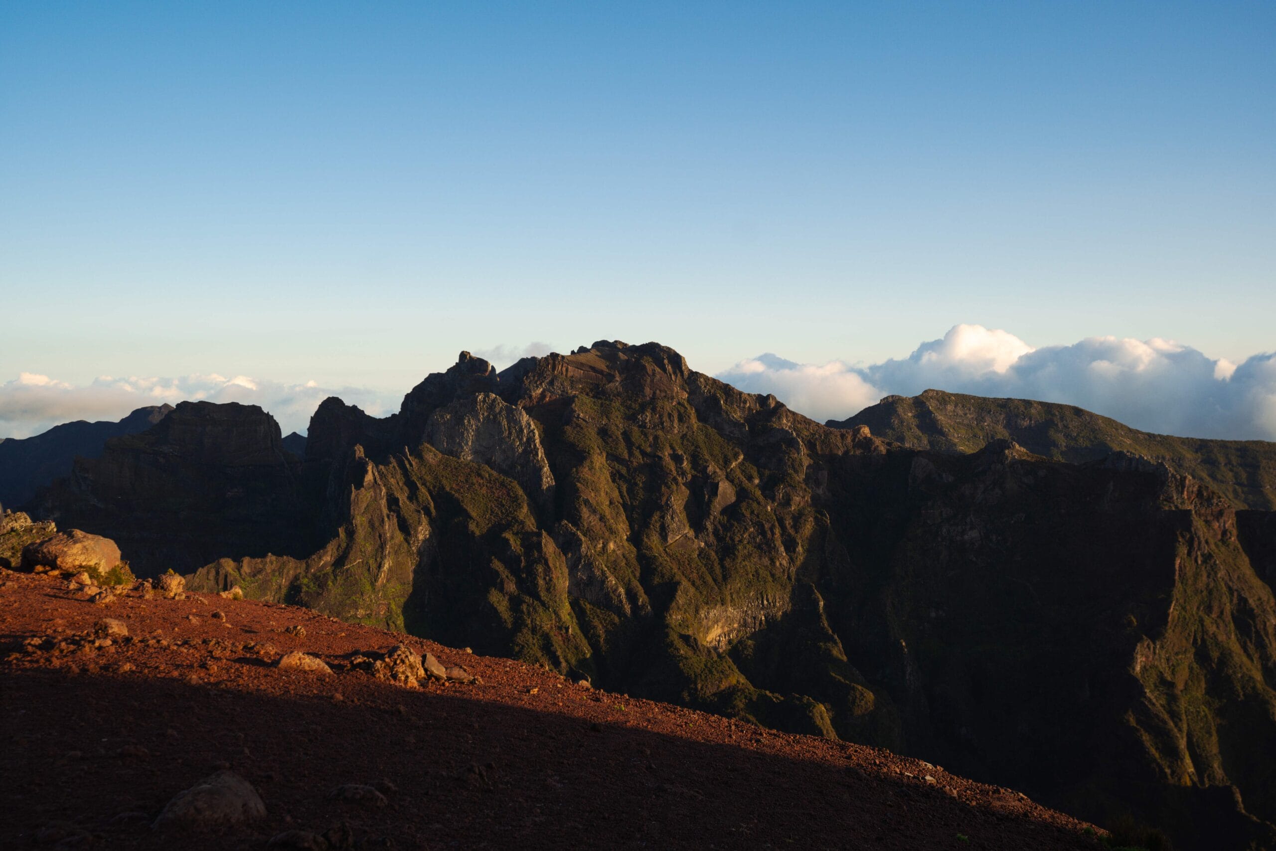 Mountain range under a clear blue sky, with rugged peaks emerging from lush greenery. One of the many things to see and do in Madeira Portugal