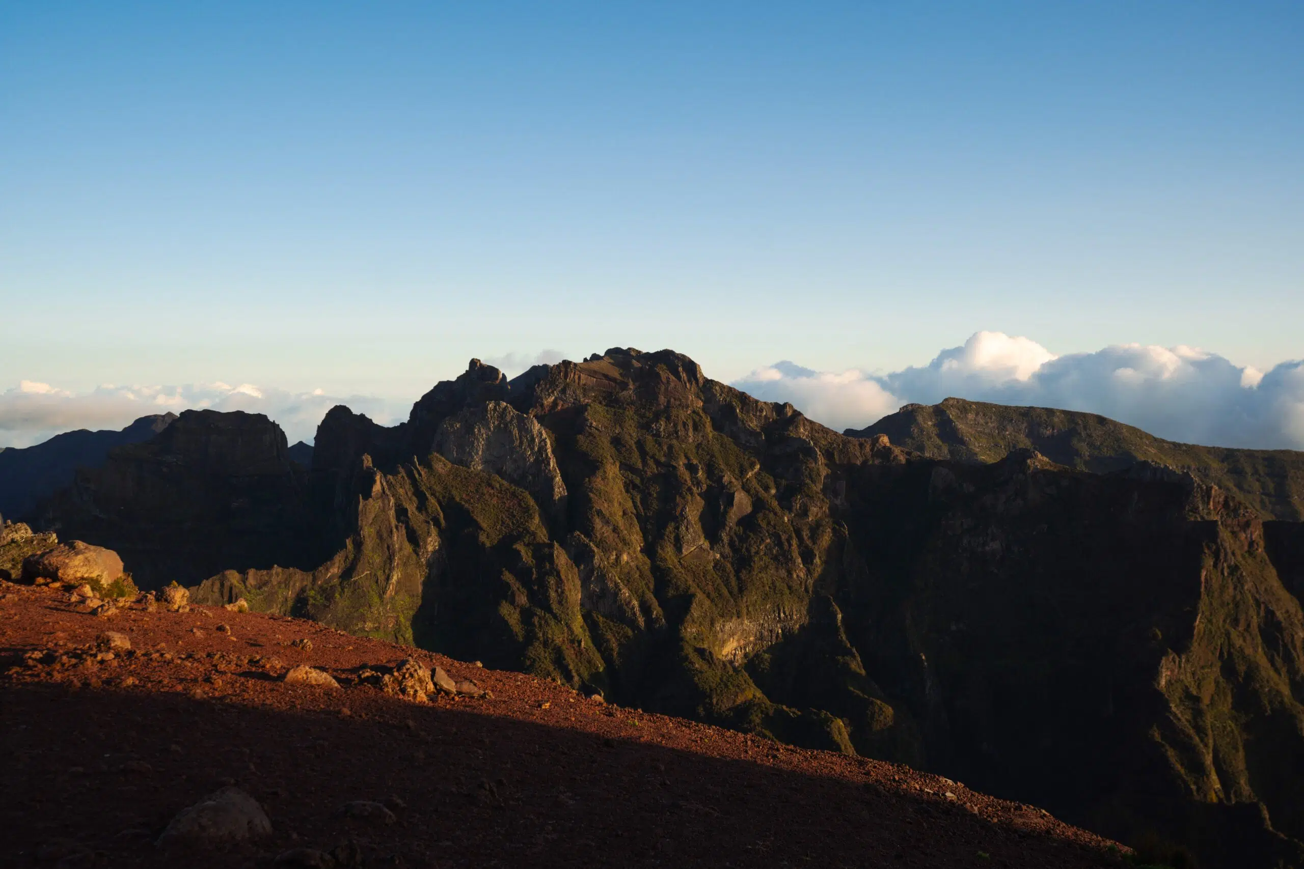 Mountain range under a clear blue sky, with rugged peaks emerging from lush greenery. One of the many things to see and do in Madeira Portugal