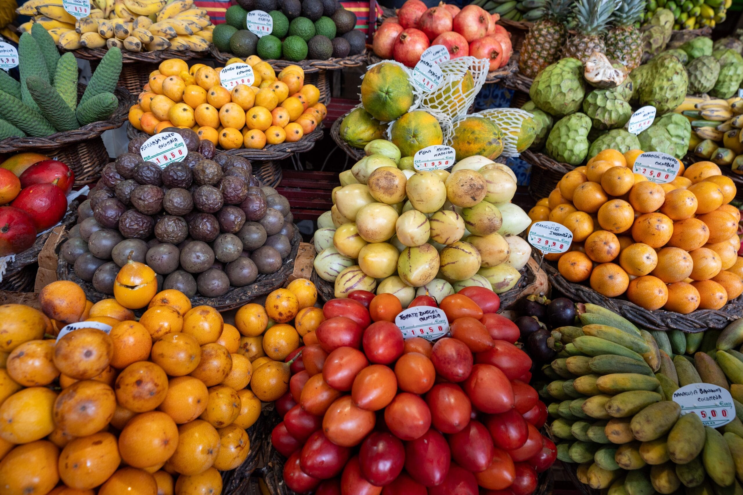 A vibrant market stall displaying a variety of fresh fruits, including oranges, avocados, papayas, and bananas, neatly arranged in wicker baskets.