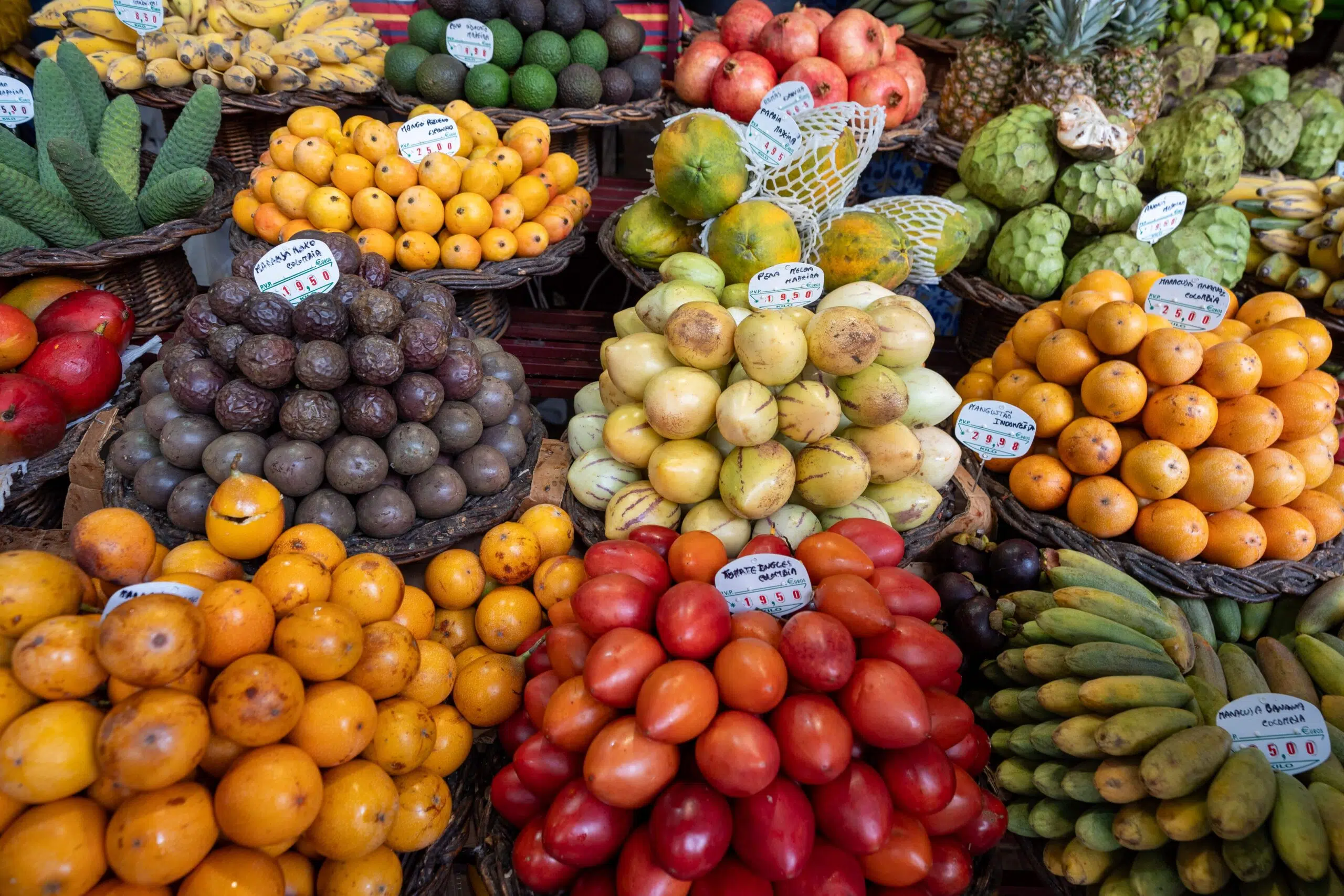 A vibrant market stall displaying a variety of fresh fruits, including oranges, avocados, papayas, and bananas, neatly arranged in wicker baskets.