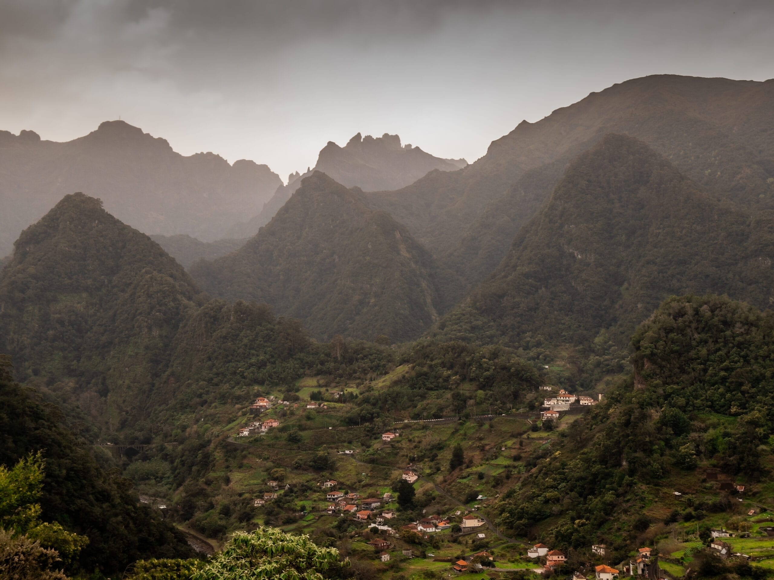 Mountainous landscape in Madeira Portugal under overcast skies, with lush green hills and a small village nestled in the valley, conveying a serene, tranquil atmosphere.