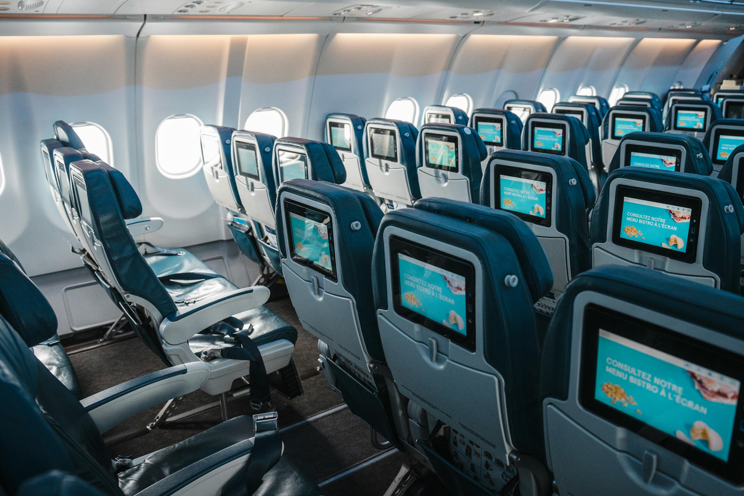 Empty airplane interior highlighting rows of seats with touchscreens, offering a modern in-flight experience.