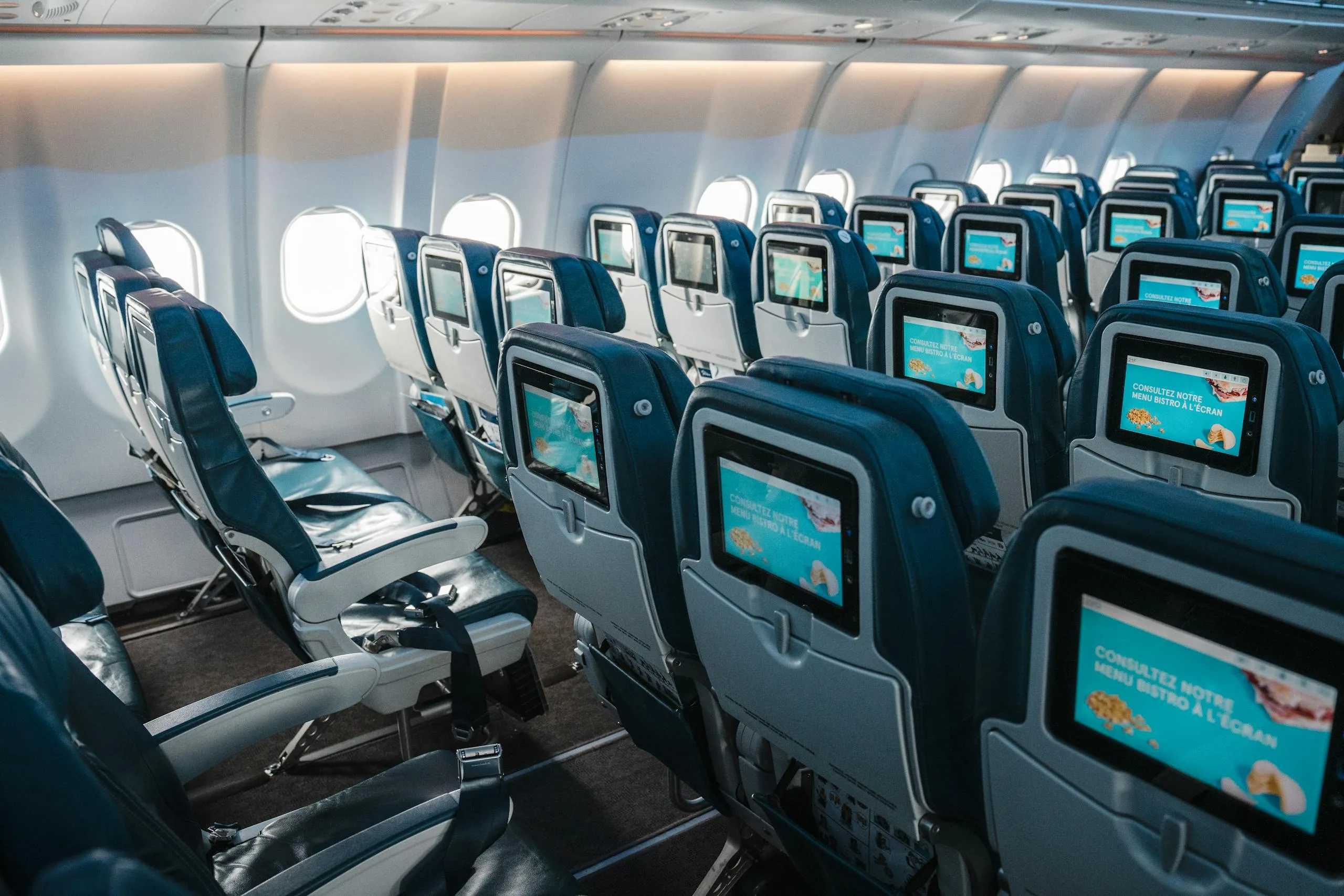 Empty airplane interior highlighting rows of seats with touchscreens, offering a modern in-flight experience.