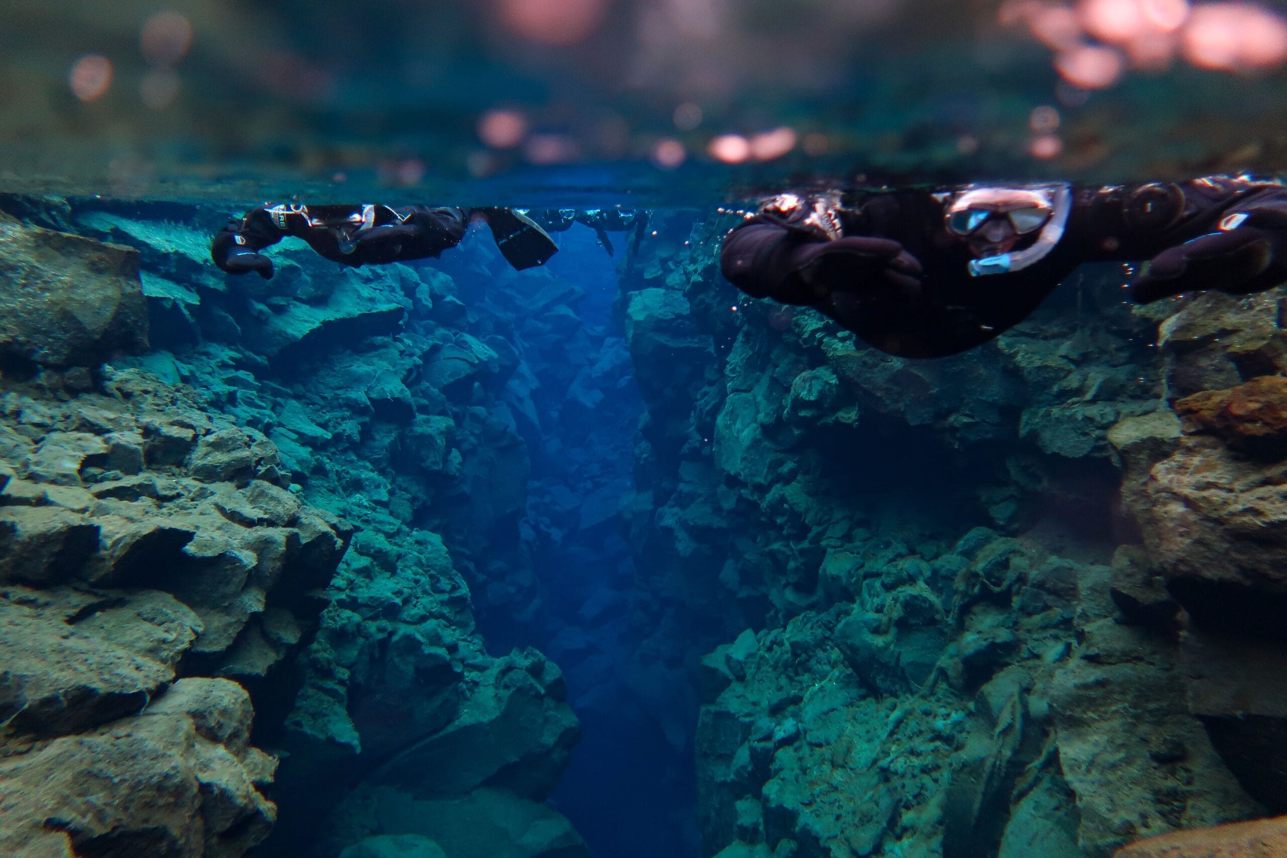 Two snorkelers floating in crystal-clear blue water between rocky crevices in Silfra, Iceland, creating a serene and adventurous atmosphere.