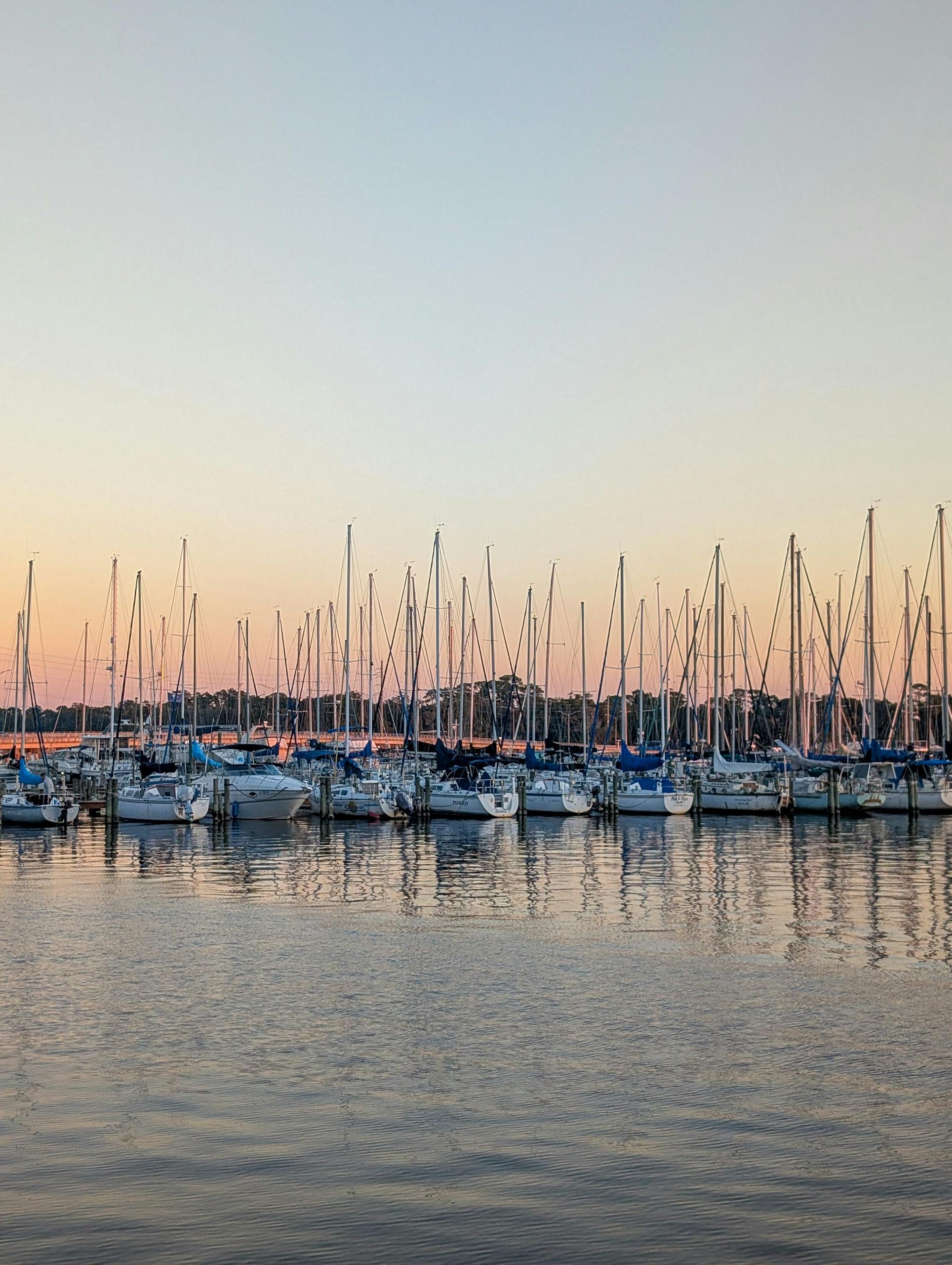 A serene view of sailboats at sunset in Jacksonville, Florida, with a calm water reflection.
