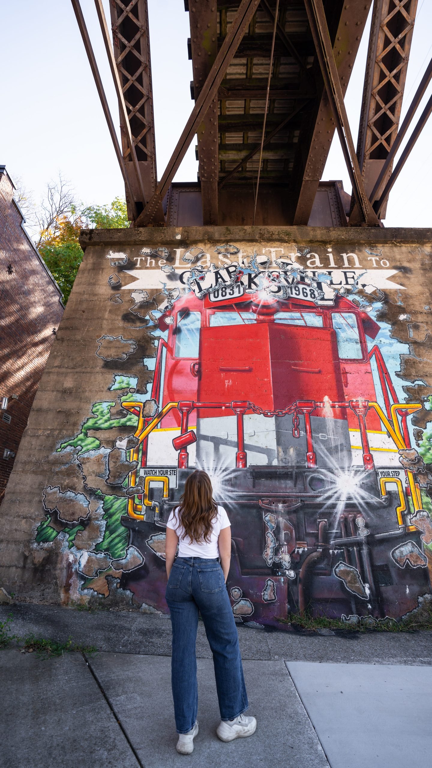 Woman standing in front of the Last Train to Clarksville mural under the old railroad bridge in Clarksville, TN