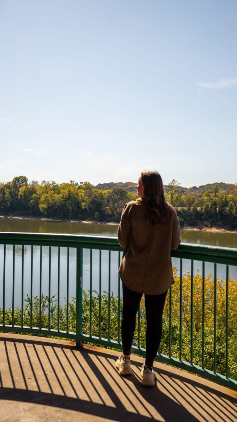 Woman looking out over the Cumberland River from a green railing on the Clarksville Riverwalk on a day trip from Nashville