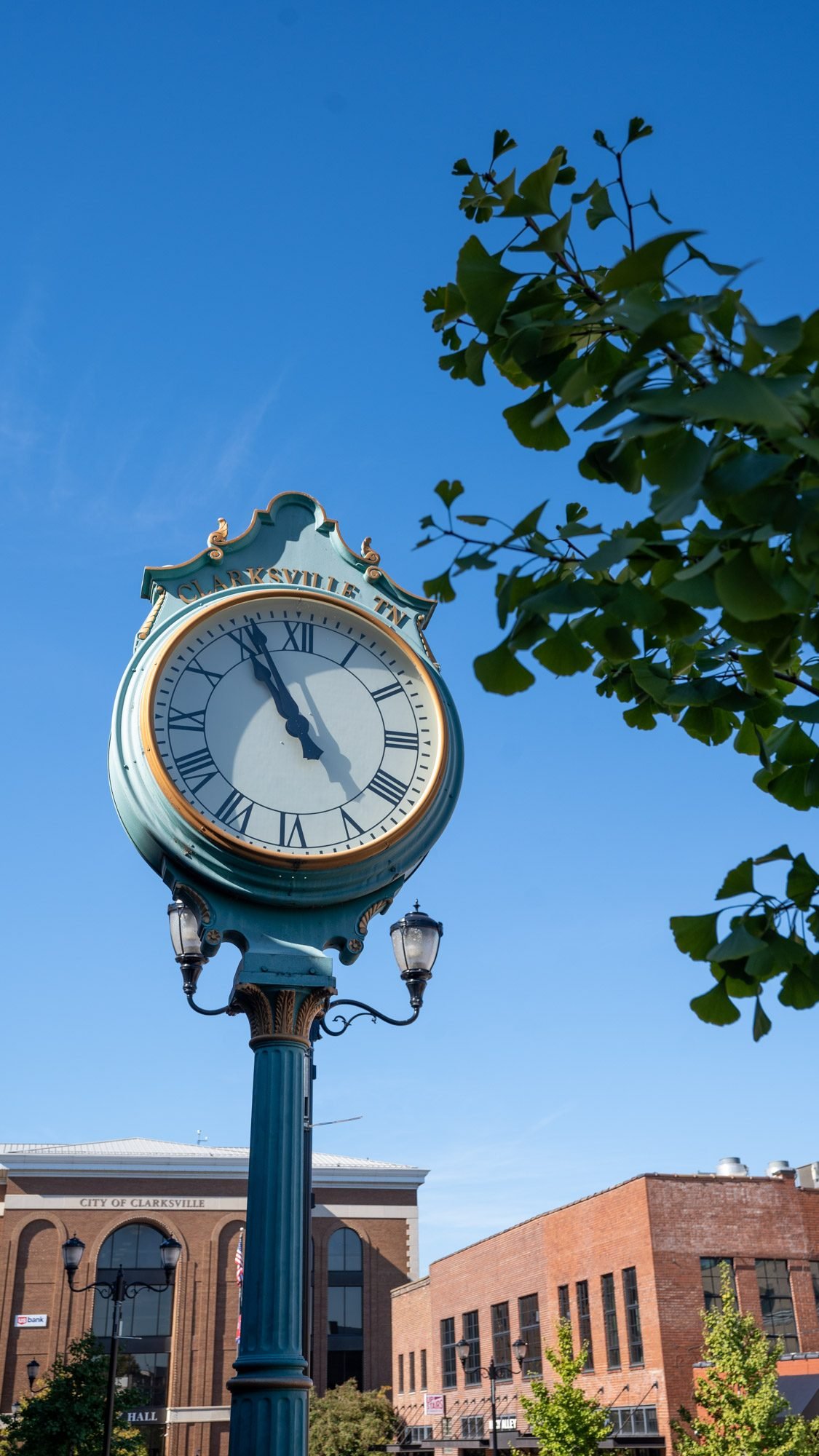 Vintage green street clock against a blue sky in downtown Clarksville
